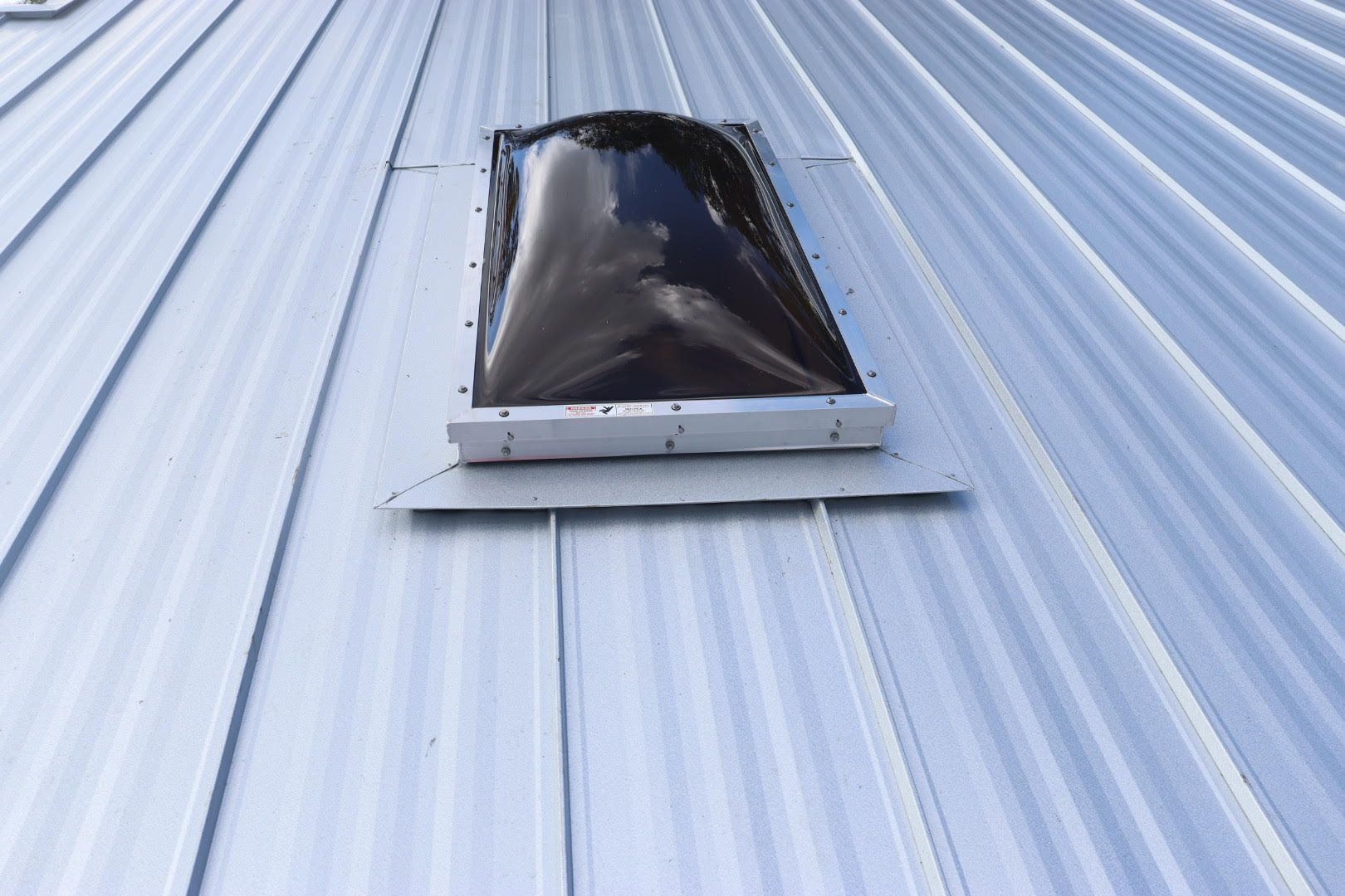 Skylight on a corrugated metal roof.  Black plastic bubble with a silver metal flashing.
