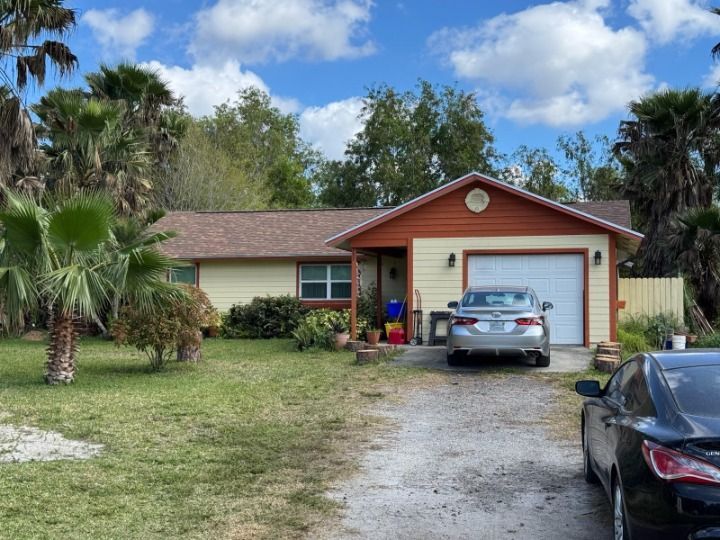 Yellow ranch home with a brown roof and garage; car parked in the driveway.