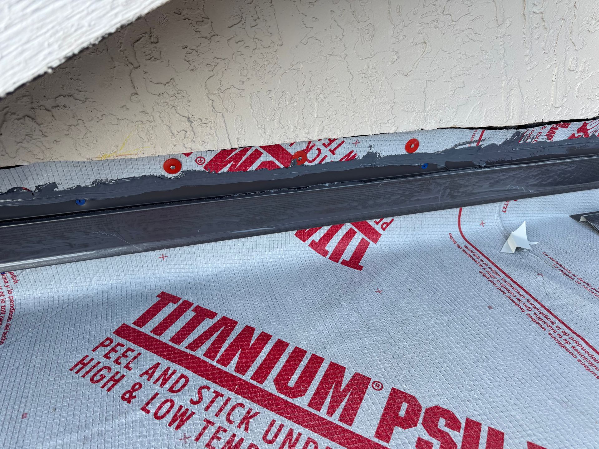 Close-up of roof flashing over red-printed roofing underlayment; the roof is near the exterior wall.