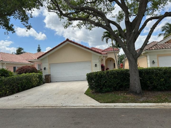 Single-story house with a white garage door, red tile roof, and a tree in front.