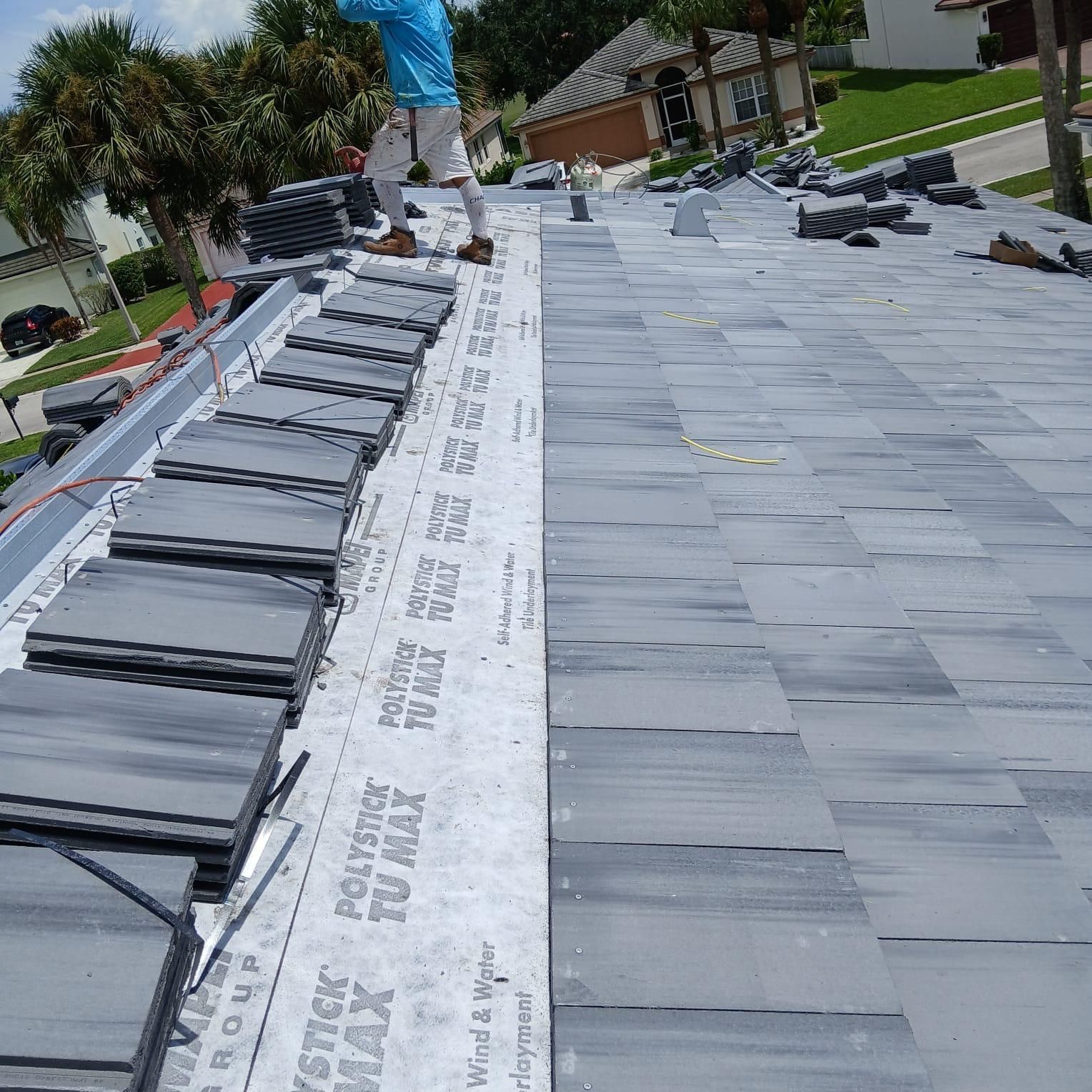 Roofers installing gray roof tiles on a house roof.