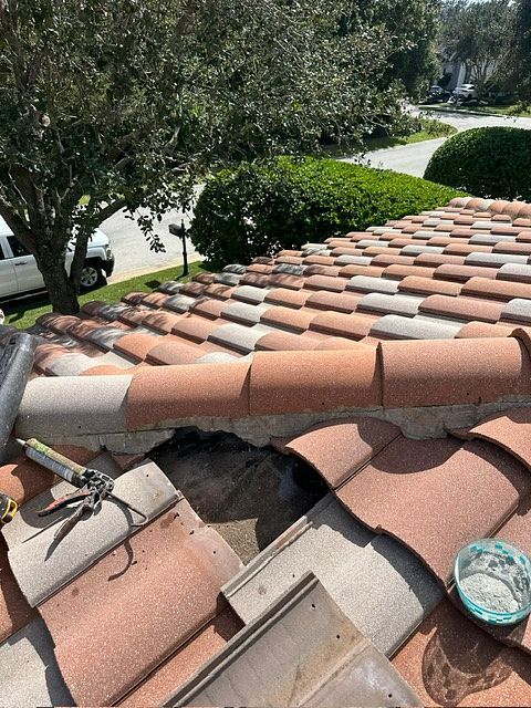 Clay tile roof with missing tiles, showing a repair in progress; daylight.