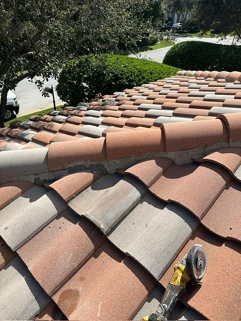 Clay roof tiles, some red, some gray, with a power tool resting on the roof, likely repair work.