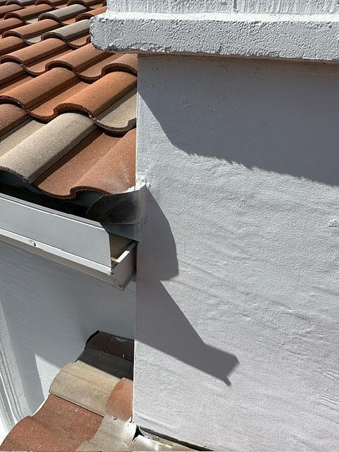 Close-up view of a white stucco wall next to a terracotta tile roof and a white gutter.