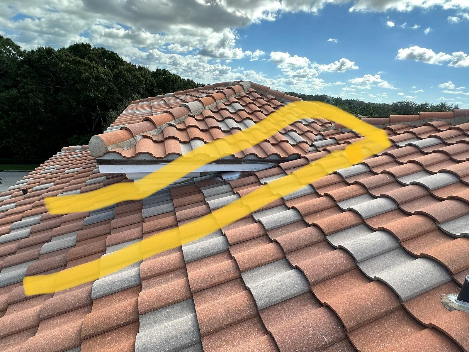 Orange and gray tile roof with yellow highlight around a vent area, against a partly cloudy sky.