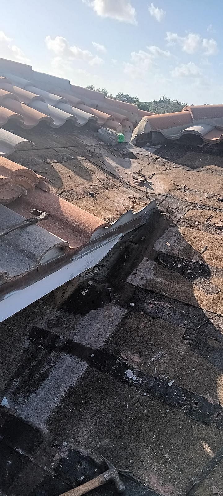 View of a tiled roof with damage, showing brown and gray tiles, a bright sky in the background.