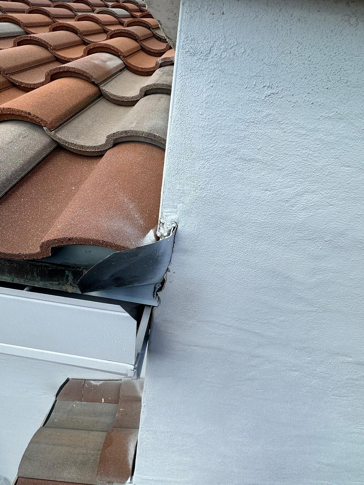 Close-up of terracotta roof tiles meeting a stucco wall, with a metal gutter visible.