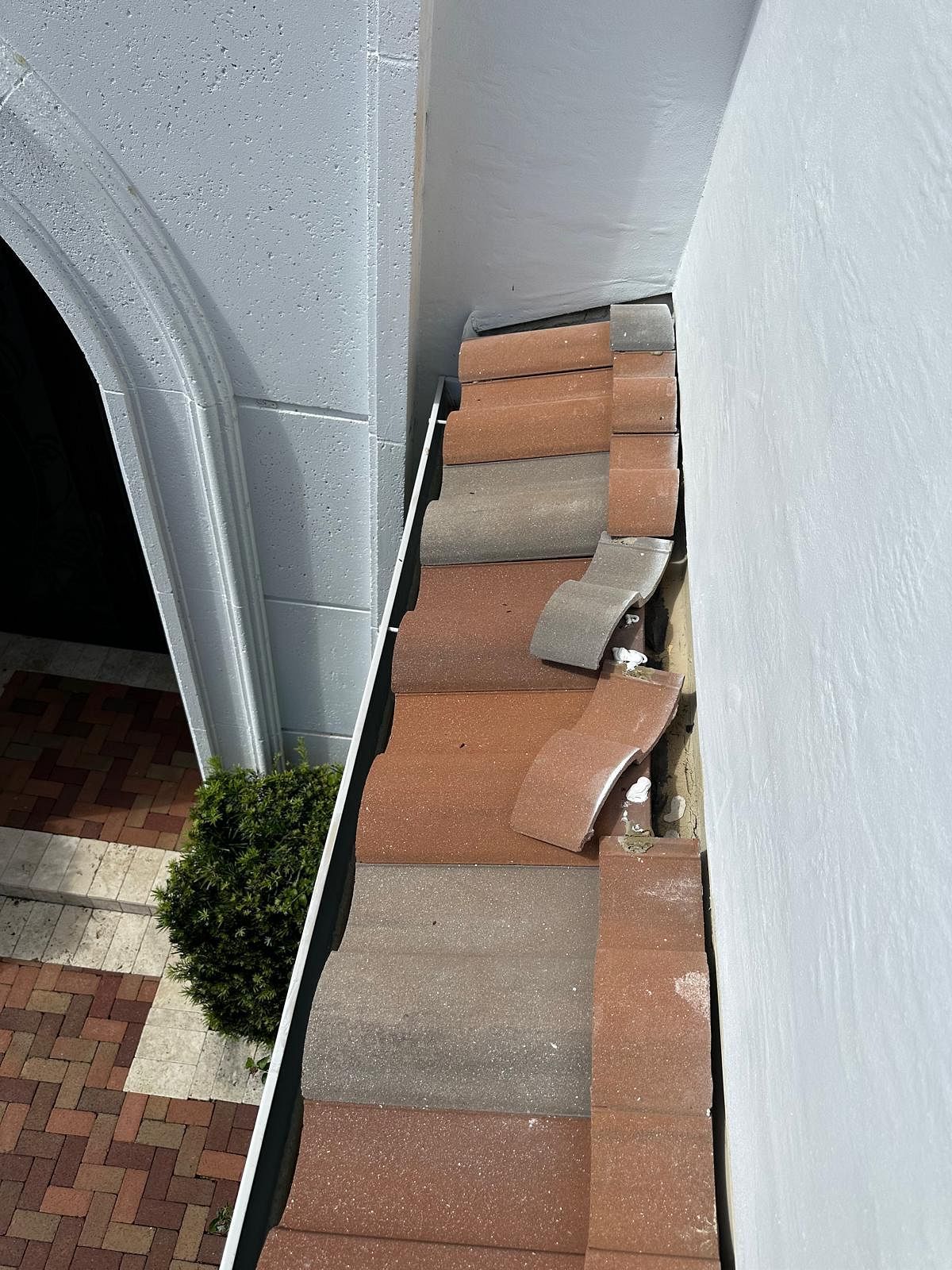 Red and gray tiles in disrepair along a wall and under an archway, part of a building's facade.