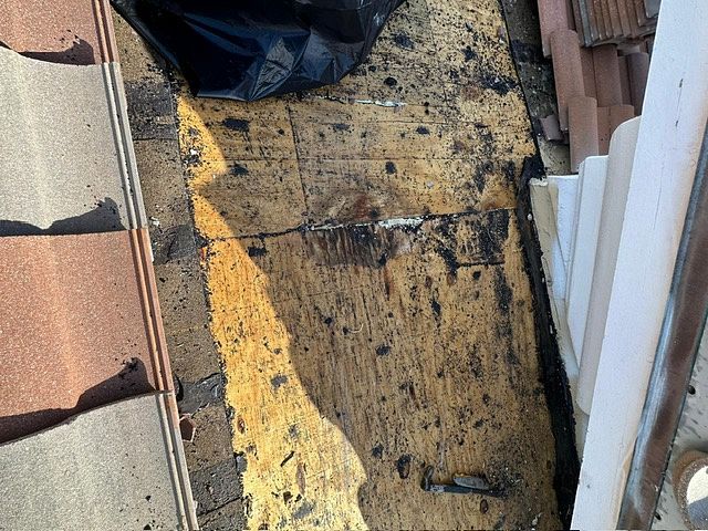 Damaged roof area with exposed wood, debris, and stacked tiles.
