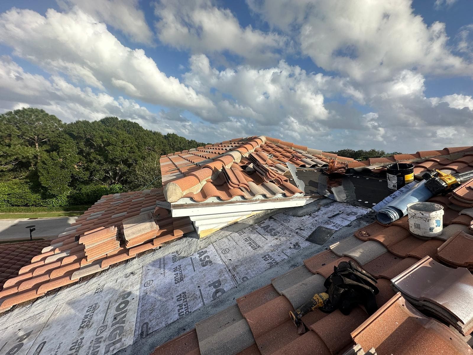 Damaged terracotta tile roof with exposed underlayment, cloudy sky.