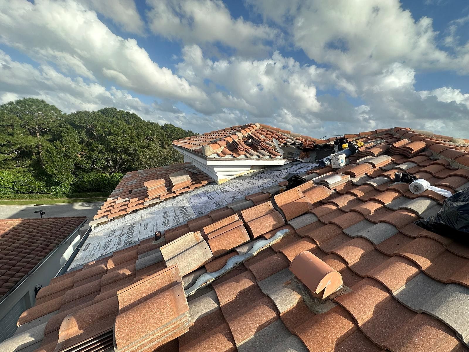 Red tile roof being repaired on a sunny day. Blue sky with clouds in the background.