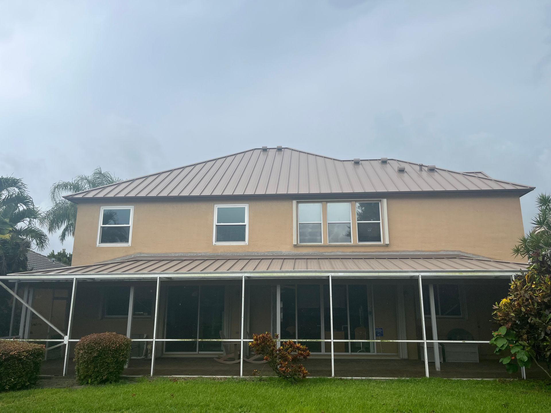 Tan two-story house with screened-in porch under a cloudy sky.