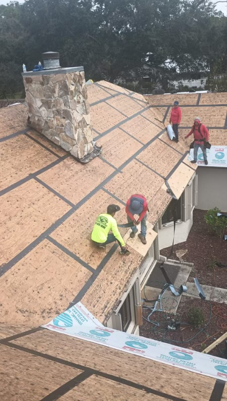 Roofers working on a house roof, laying wood paneling. Overcast day.