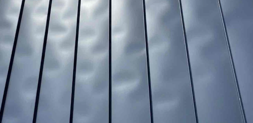 Vertical metallic blinds reflect the sky, creating alternating stripes of light and shadow.