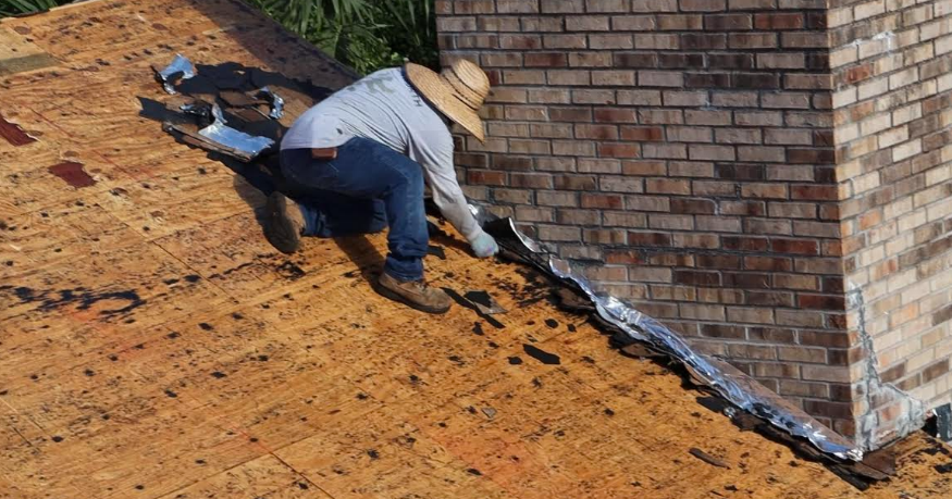 Roofer installing flashing around a brick chimney on a sloping roof.