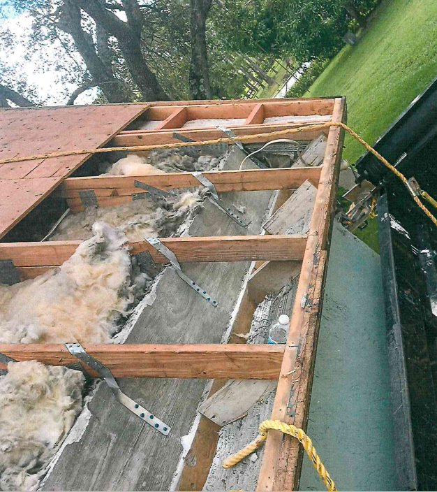 View of a damaged roof. Wood frame, insulation, and debris visible. Yellow rope attached to the edge.