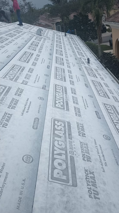 Roof with Polyglass underlayment being installed, with workers in the background.