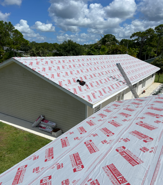 A house with a roof covered in red-labeled underlayment; a ladder leans against the roof.