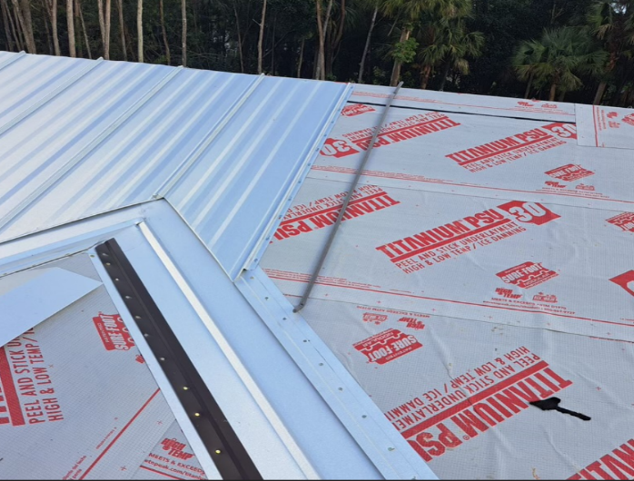 Metal roof installation: silver panels, red underlayment, construction scene.