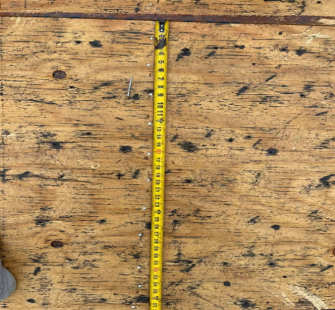 Yellow tape measure on a wooden surface, measuring a rusty metal bar.