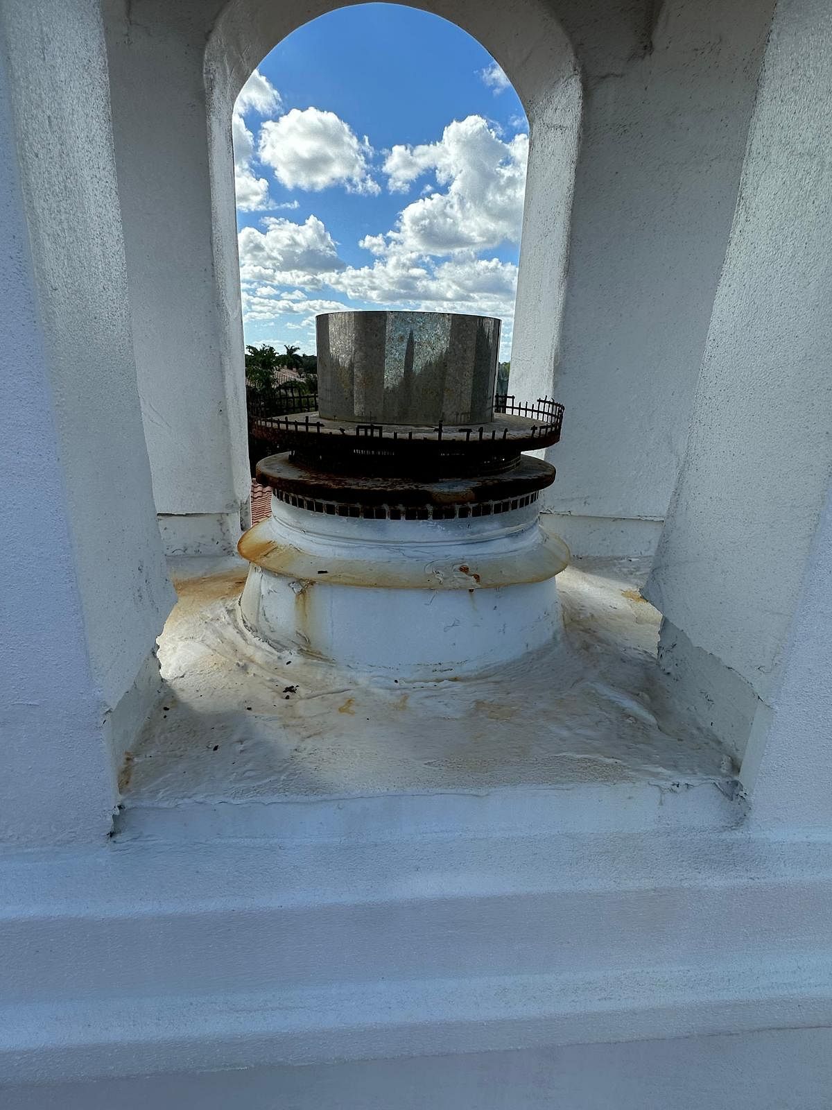 White arched opening frames a weathered metal structure against a blue sky with clouds.