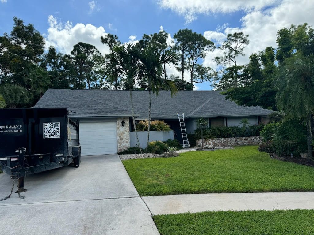 House with new gray roof, white garage door, on a sunny day with blue sky and trees.