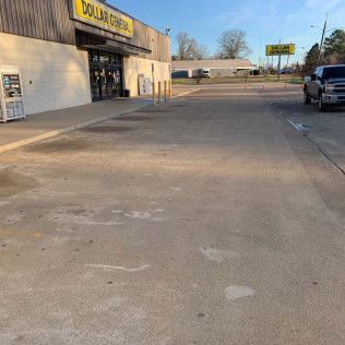 Dollar General store, concrete lot. Building has black doors, yellow sign. Pickup truck parked nearby.