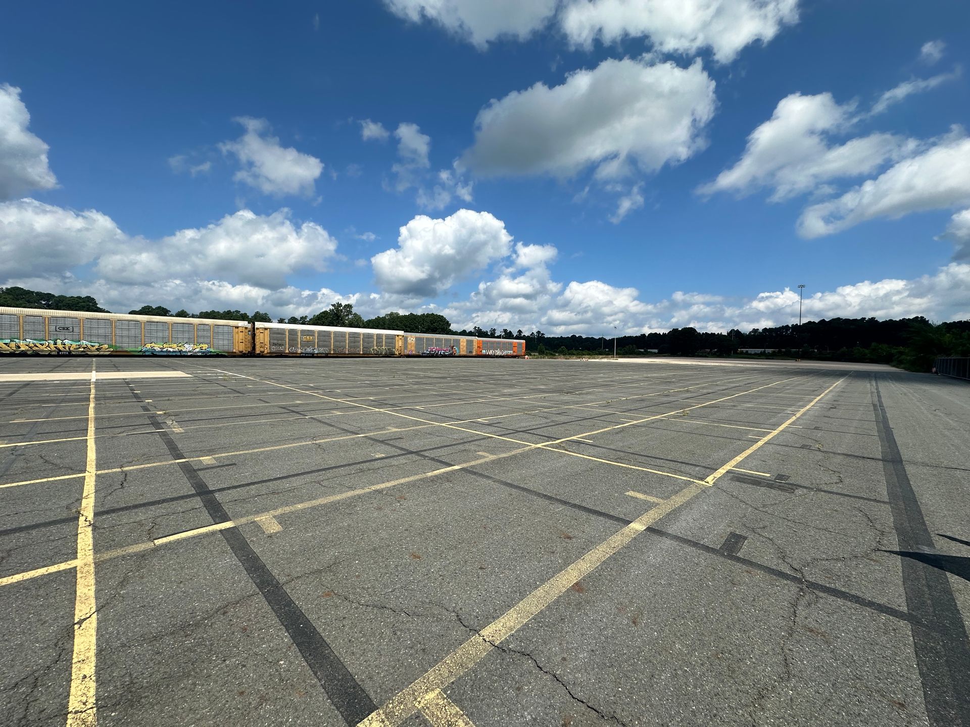 Empty asphalt parking lot under a partly cloudy blue sky.