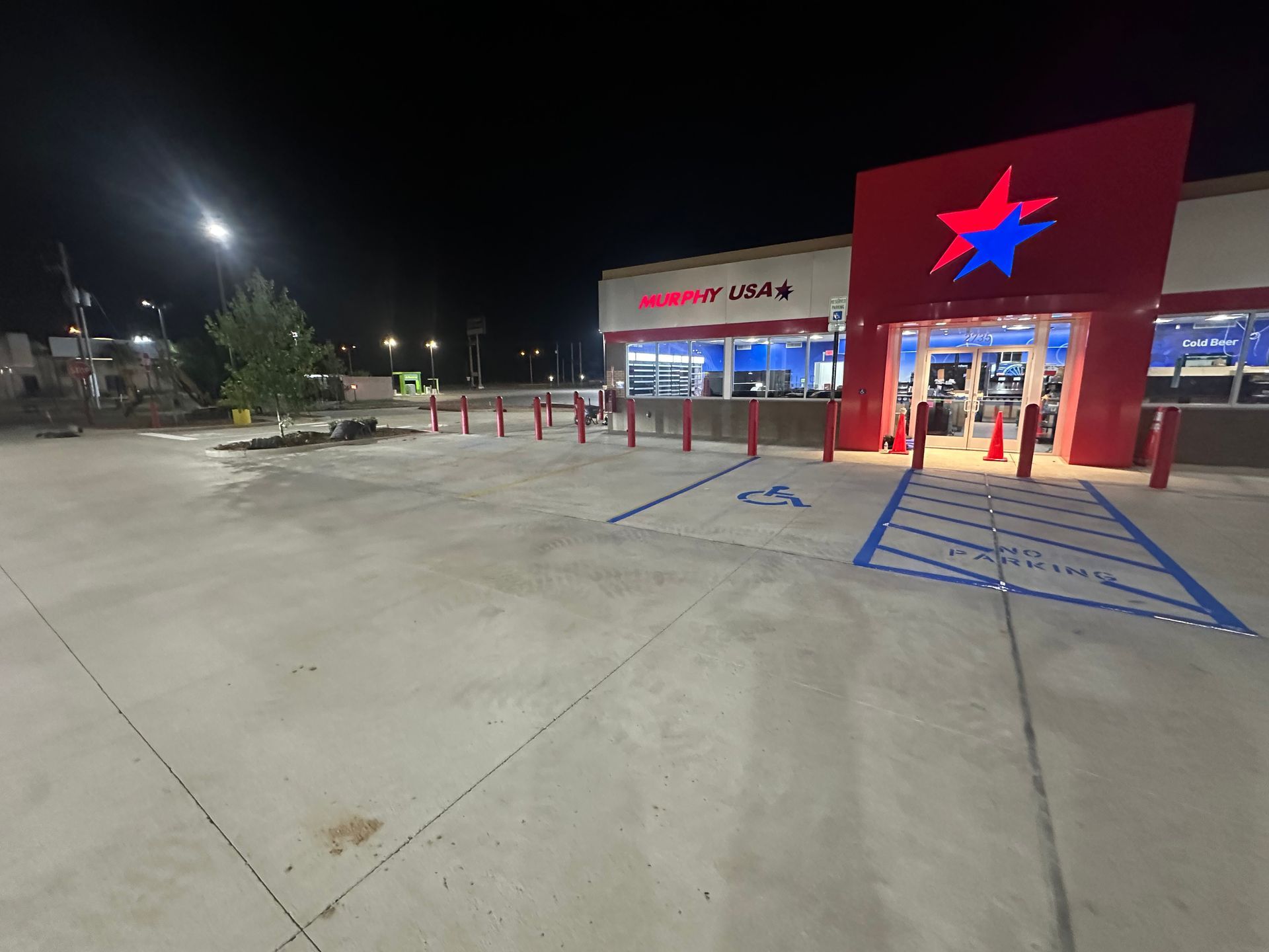 A convenience store at night, with a red and blue star logo. Concrete parking lot, wheelchair accessible.