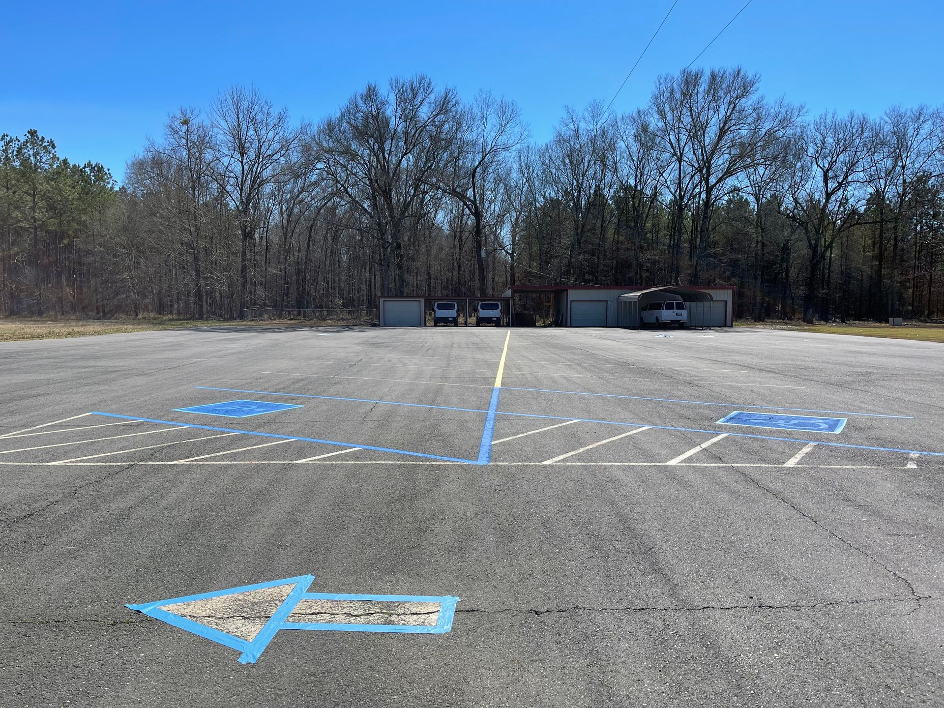 Asphalt area with blue directional arrow and painted parking markings. Buildings and trees in background.