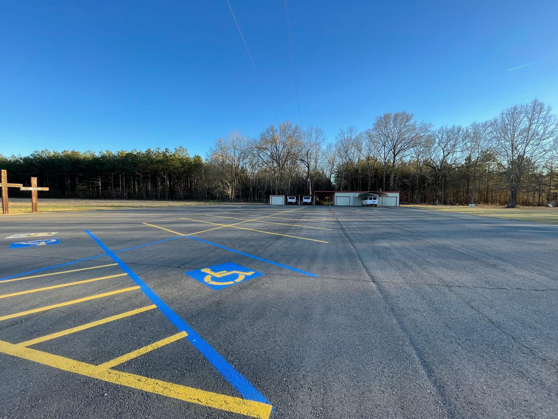 Empty parking lot with blue handicap symbols and yellow lines. Trees and a blue sky in the background.