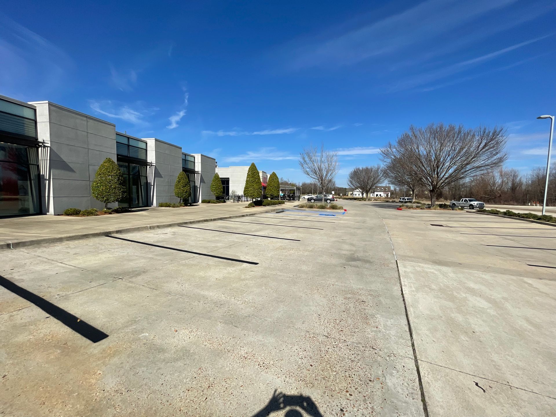 Wide view of a concrete parking lot in front of a light-colored building under a bright blue sky.