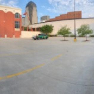 An empty parking lot in front of buildings, with a classic green car parked.