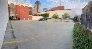 Empty parking lot with a green car, buildings, and a city skyline in the background.