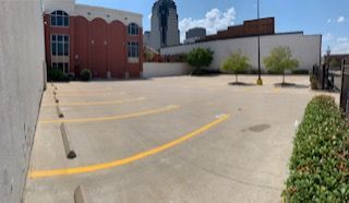 Empty parking lot in an urban setting, with yellow lines. Buildings and a tall skyscraper in the background.