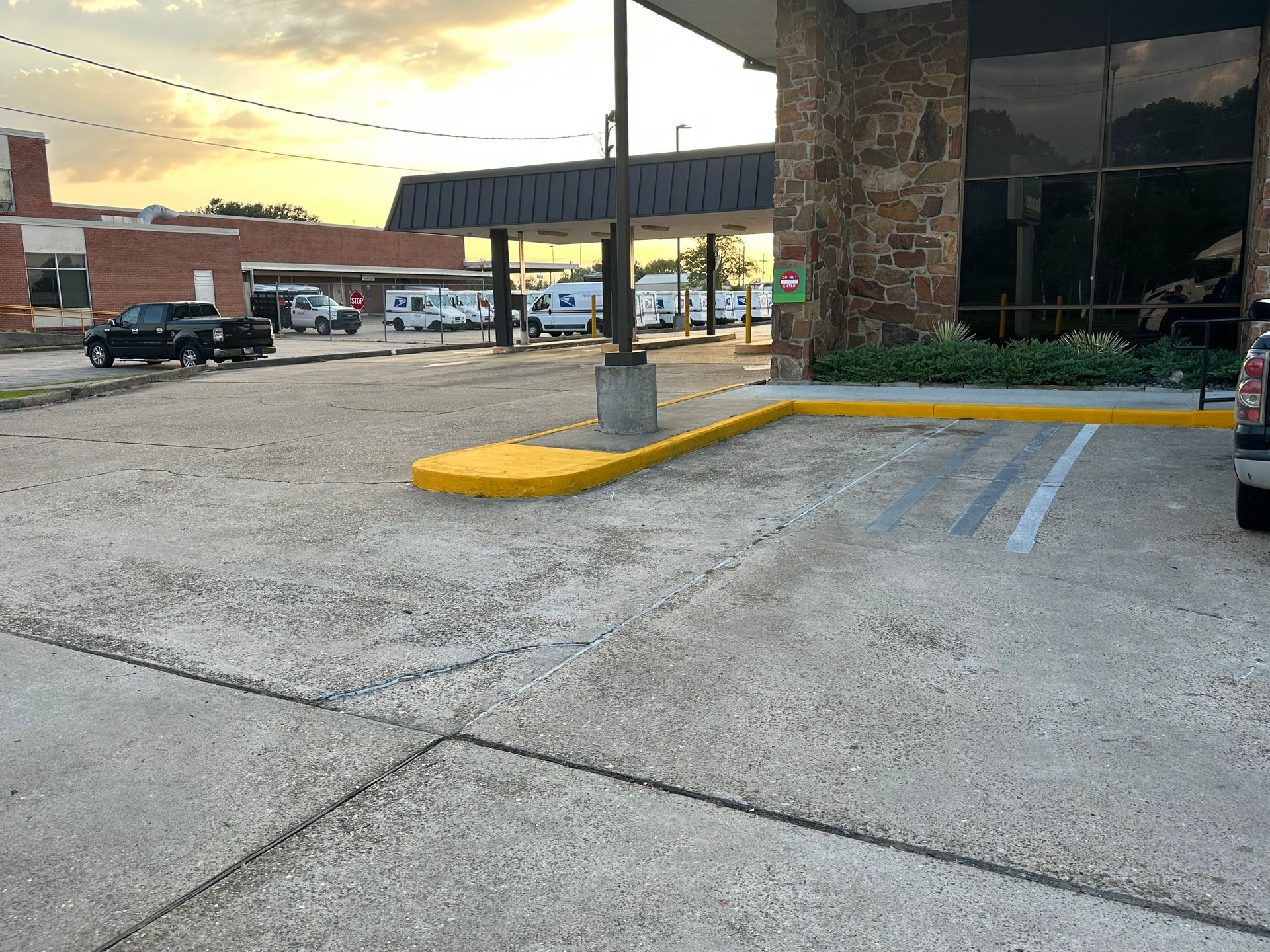 Parking lot with vehicles and building. Yellow curb and concrete surface. Sky with sunset colors.