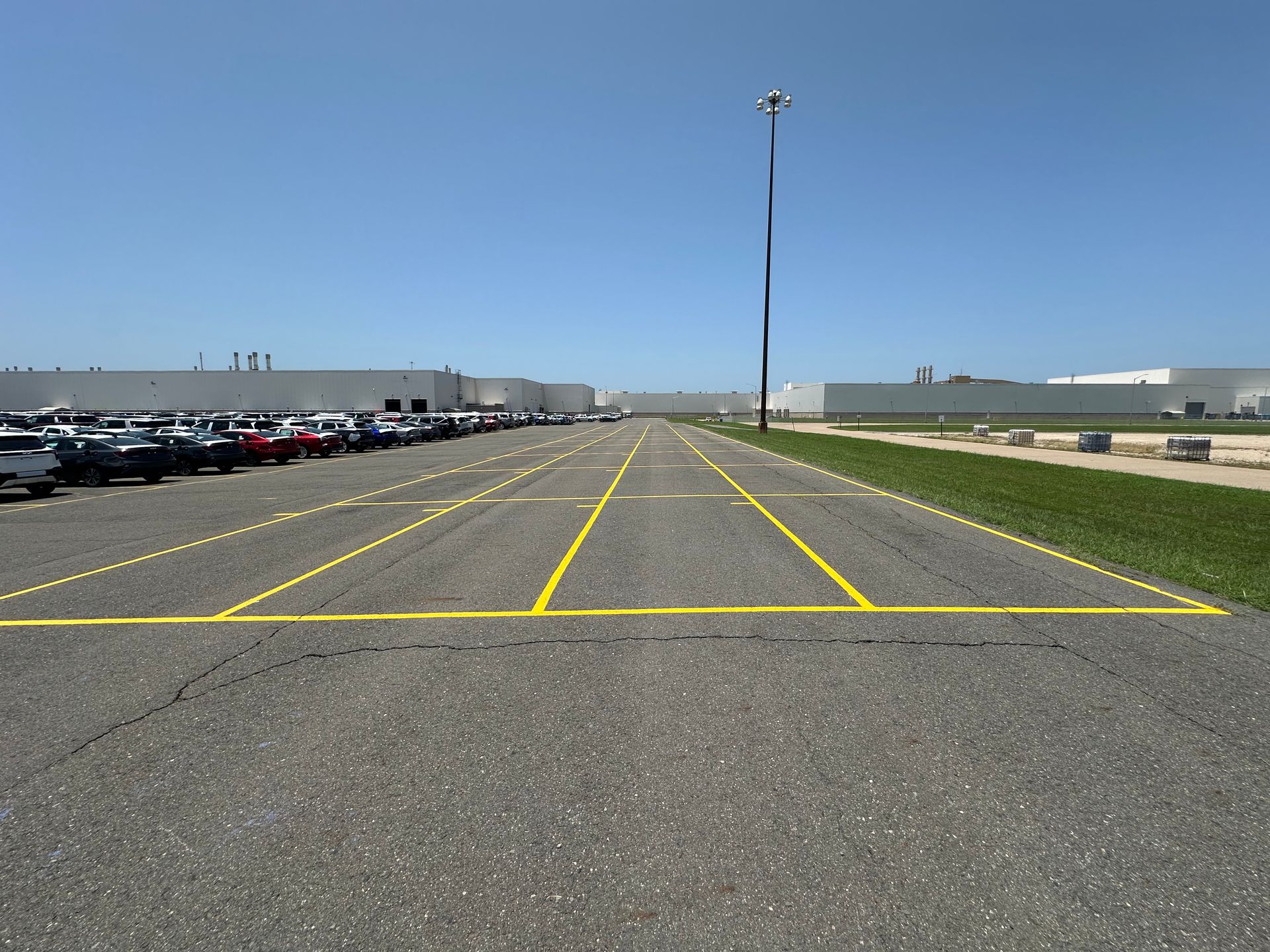 Asphalt lot with yellow lines and parked cars; factory buildings and blue sky.