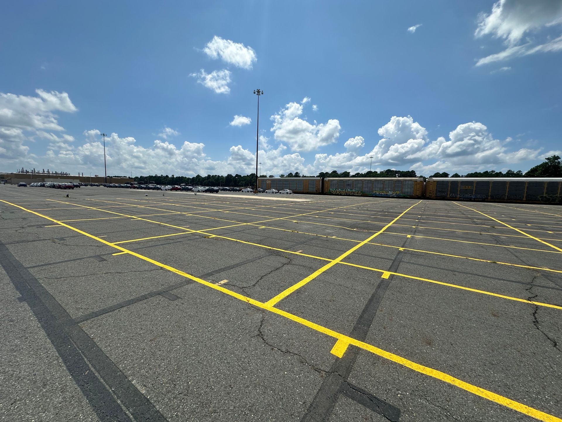 Empty parking lot with yellow painted lines under a partly cloudy, blue sky.