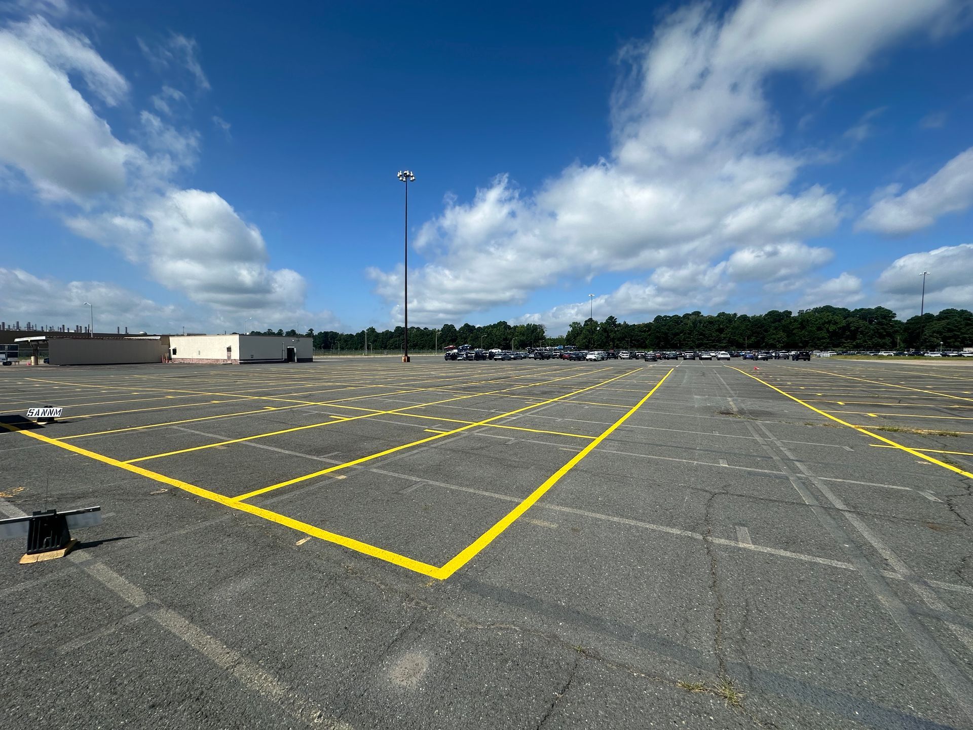 Empty parking lot with new yellow painted lines, under a blue sky with clouds.