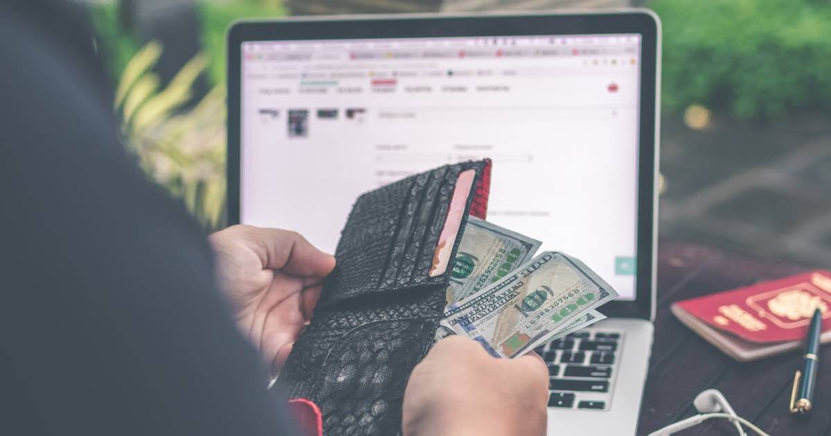 a person is holding a wallet full of money in front of a laptop computer .
