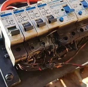 Damaged electrical circuit breaker panel with melted plastic and exposed wires.