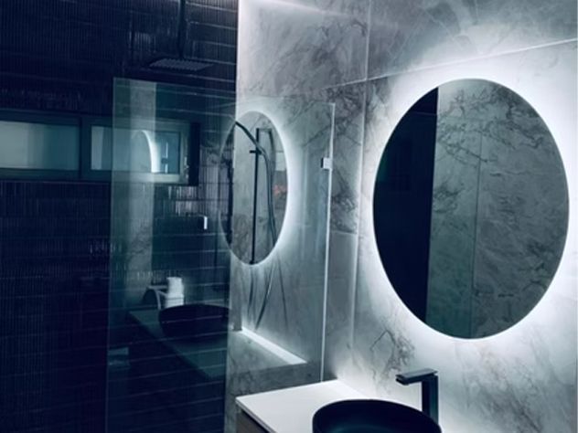 Modern bathroom with grey marble walls, two circular mirrors with LED backlighting, and a black sink.