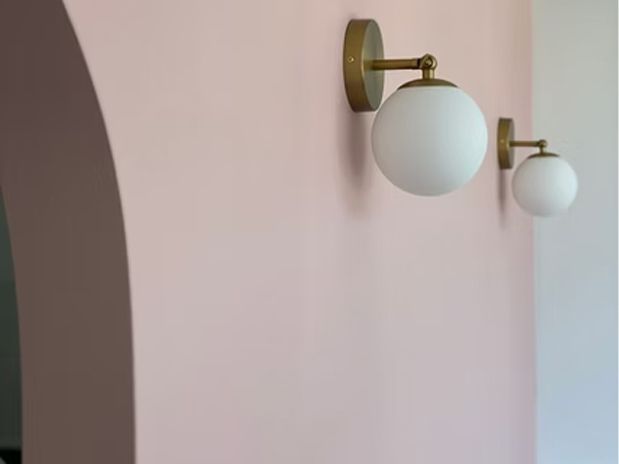 Two globe-shaped white lamps with brass fixtures mounted on a pink wall next to an archway.