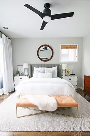 Bedroom with a bed, white bedding, gray walls, rug, bench, and ceiling fan.
