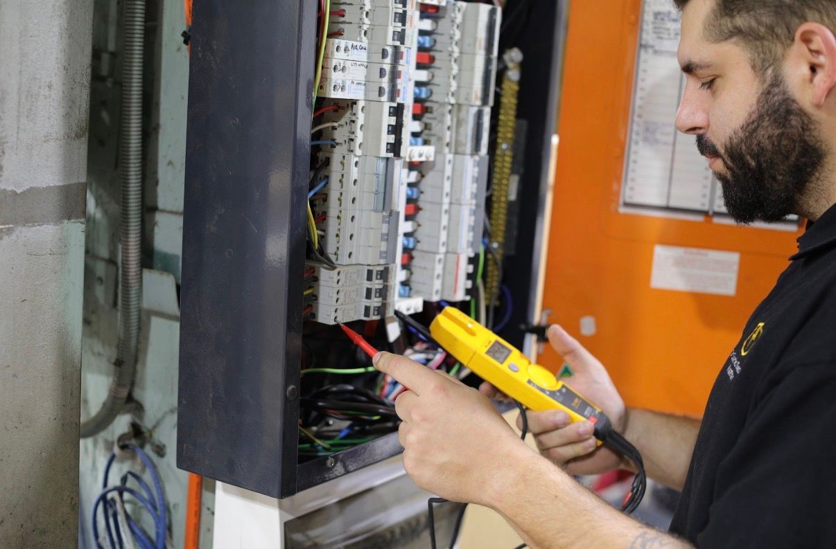 Electrician in black shirt with logo, working on electrical panel, wearing gloves.
