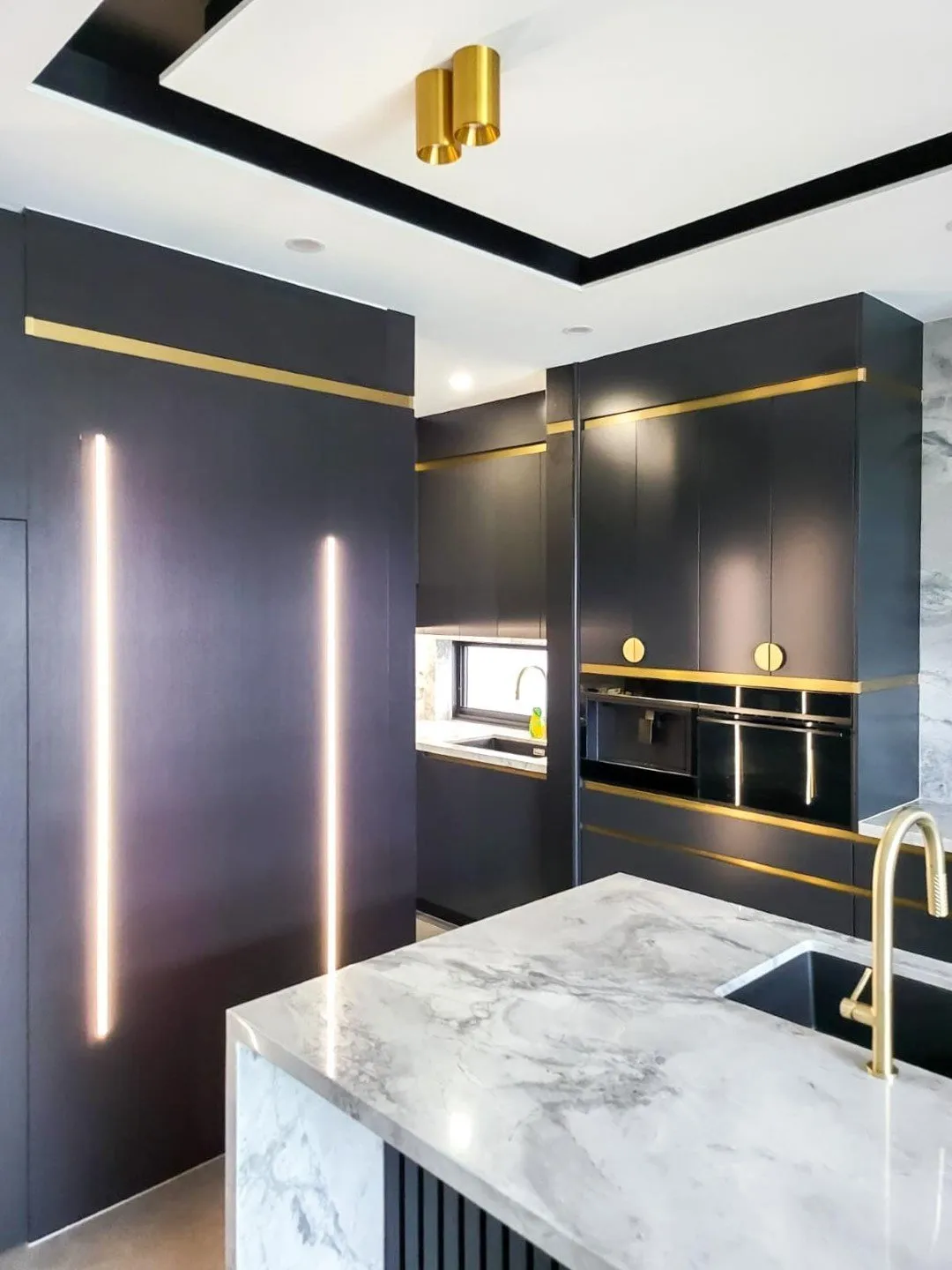 Modern kitchen with white island, black cabinets, copper pendant lights, and patterned rug.