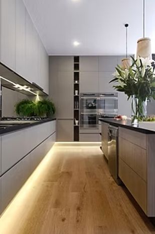 Modern kitchen with grey cabinets, wood floor, and island. Under-cabinet and floor lighting.
