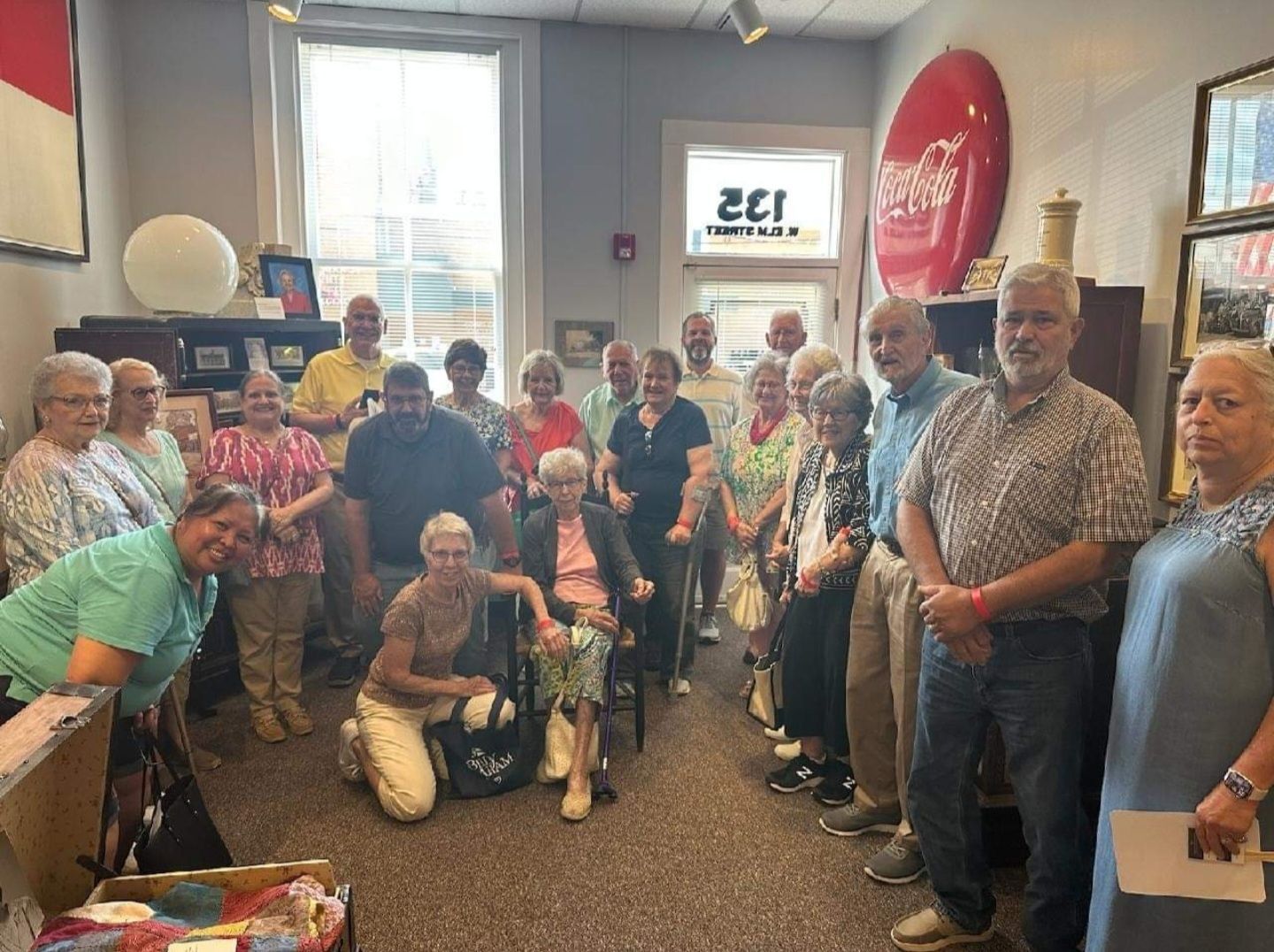 A group of people standing and sitting together for a photo in a room with store decor, including a large red sign.