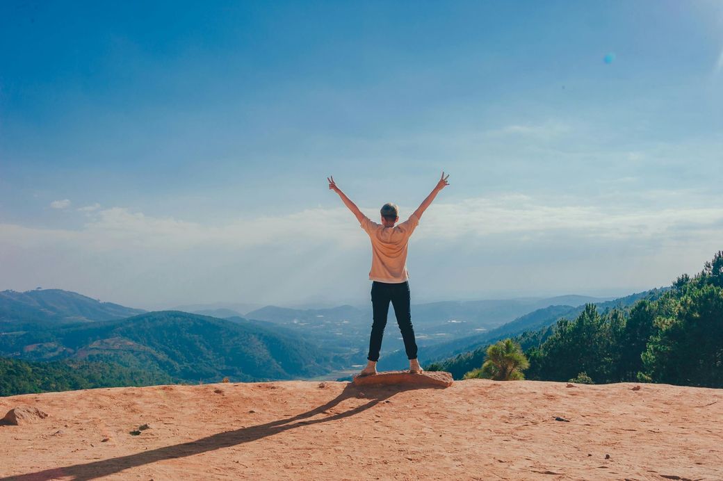 Person with arms raised on a hilltop, overlooking mountains and sky.