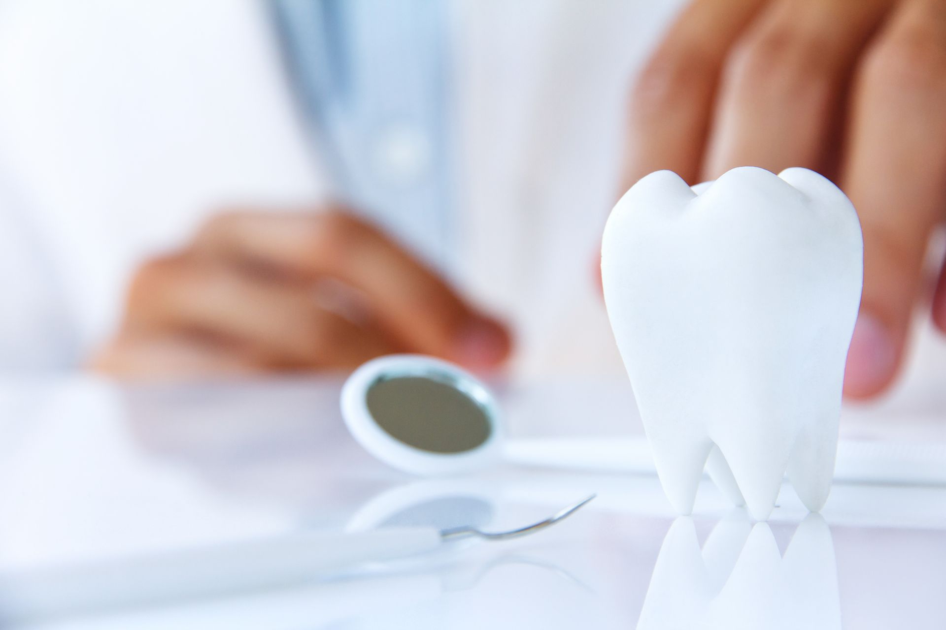 White dental tooth model beside a mirror and blurred hands in a clinical setting